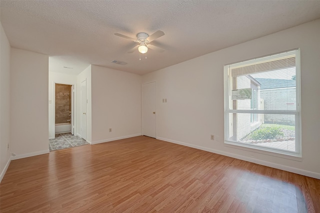 unfurnished room with ceiling fan, light wood-type flooring, and a textured ceiling