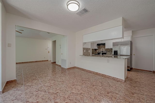 kitchen featuring kitchen peninsula, light stone countertops, white cabinets, and a textured ceiling