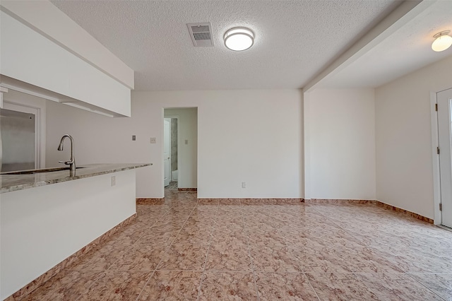 kitchen with white cabinets, sink, a textured ceiling, and stainless steel refrigerator