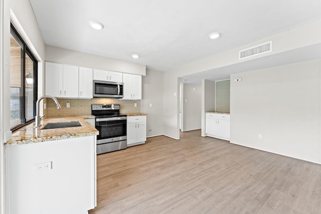 kitchen with light hardwood / wood-style floors, tasteful backsplash, stainless steel appliances, sink, and white cabinetry