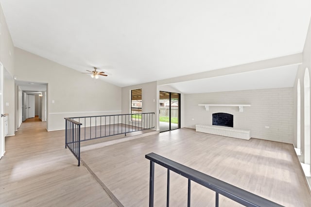 interior space with ceiling fan, lofted ceiling, a brick fireplace, and light hardwood / wood-style flooring