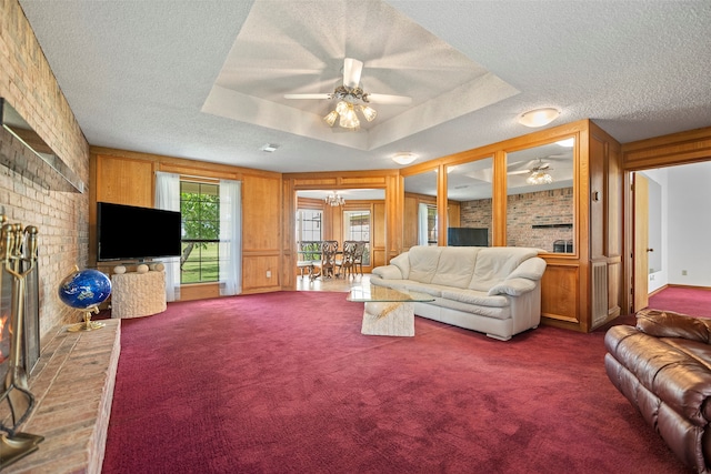 living room featuring a textured ceiling, a brick fireplace, carpet flooring, ceiling fan, and a raised ceiling