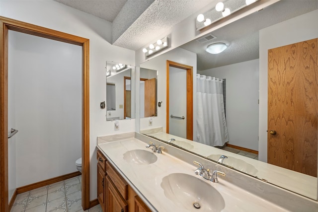 bathroom featuring toilet, tile flooring, large vanity, double sink, and a textured ceiling