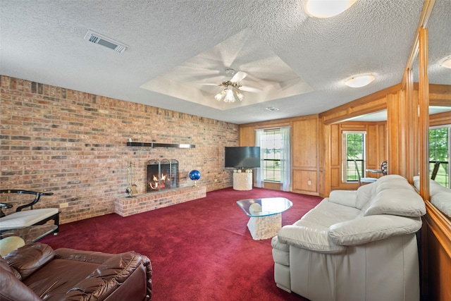 living room featuring a raised ceiling, a healthy amount of sunlight, a fireplace, and carpet flooring