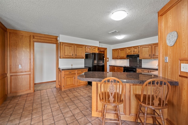 kitchen featuring a kitchen breakfast bar, a textured ceiling, black appliances, kitchen peninsula, and light tile floors