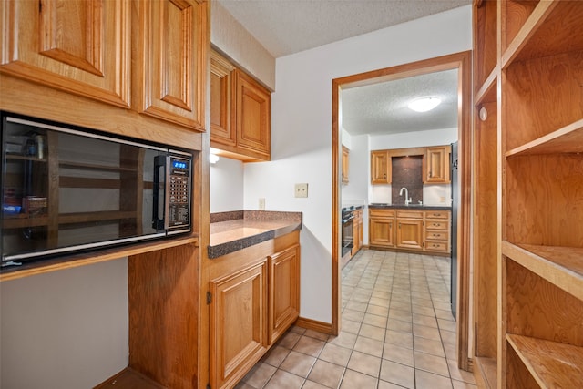 kitchen with a textured ceiling, black microwave, range, sink, and light tile flooring