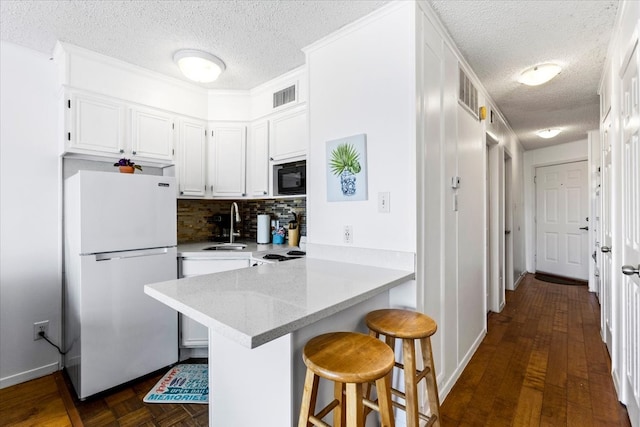 kitchen with white refrigerator, kitchen peninsula, tasteful backsplash, black microwave, and white cabinetry