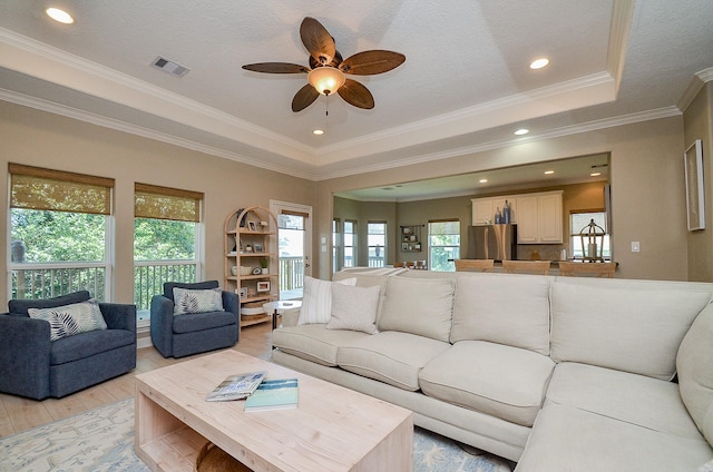 living room featuring crown molding, light wood-type flooring, a tray ceiling, and ceiling fan