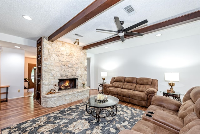 living room with a textured ceiling, a fireplace, beamed ceiling, hardwood / wood-style floors, and ceiling fan