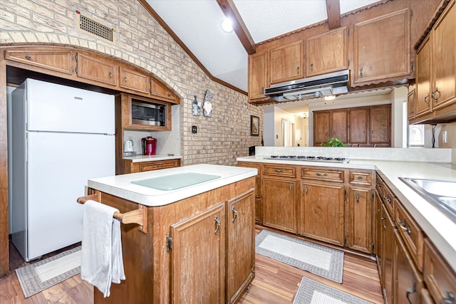 kitchen with a textured ceiling, brick wall, light wood-type flooring, appliances with stainless steel finishes, and vaulted ceiling