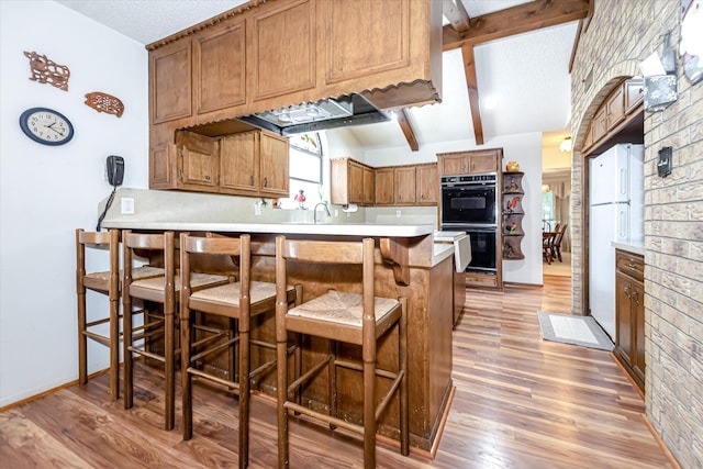 kitchen with double oven, kitchen peninsula, a kitchen bar, light wood-type flooring, and sink