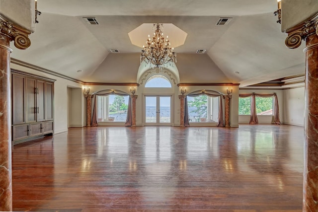 unfurnished living room with crown molding, lofted ceiling, dark wood-type flooring, an inviting chandelier, and ornate columns