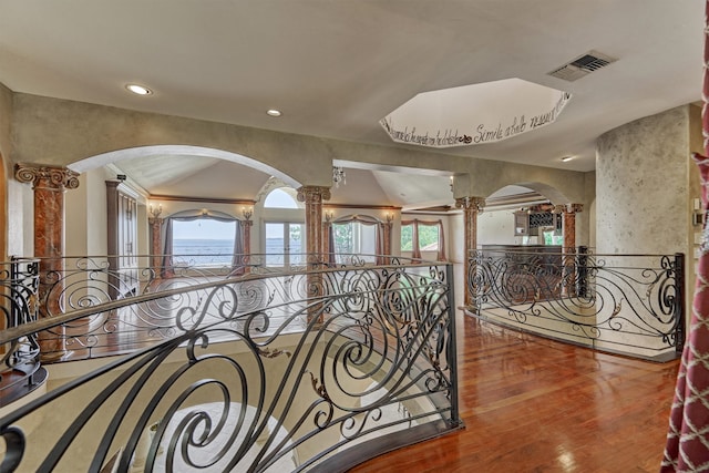 corridor with vaulted ceiling, hardwood / wood-style floors, and decorative columns