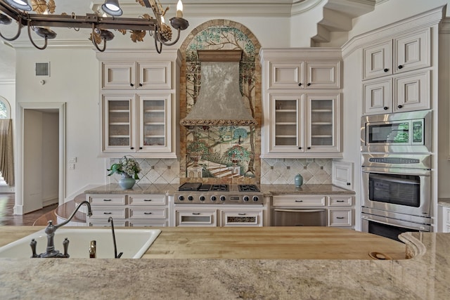 kitchen featuring premium range hood, backsplash, ornamental molding, sink, and appliances with stainless steel finishes