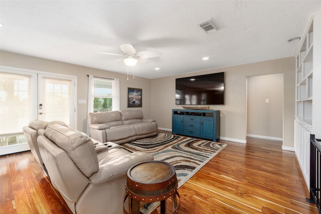 living room with light hardwood / wood-style floors, built in features, ceiling fan, a textured ceiling, and french doors