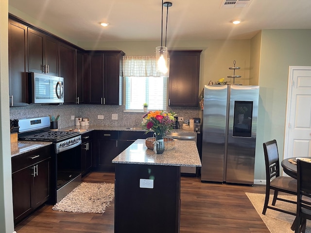 kitchen with light stone countertops, dark wood-type flooring, stainless steel appliances, decorative light fixtures, and a kitchen island