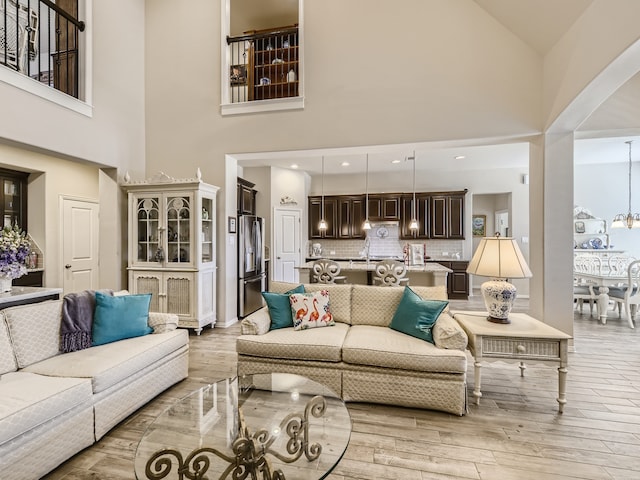 living room featuring light wood-type flooring, an inviting chandelier, high vaulted ceiling, and sink