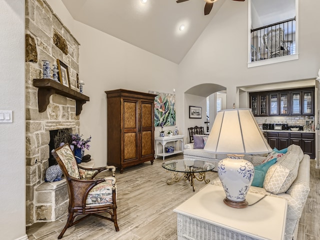 living room with light wood-type flooring, high vaulted ceiling, ceiling fan, and a stone fireplace