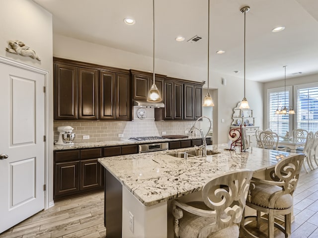 kitchen featuring a kitchen island with sink, sink, hanging light fixtures, and light hardwood / wood-style floors