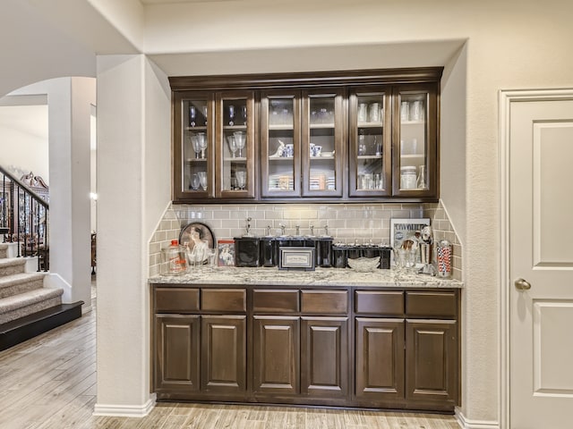 bar with dark brown cabinetry, light hardwood / wood-style flooring, and light stone counters