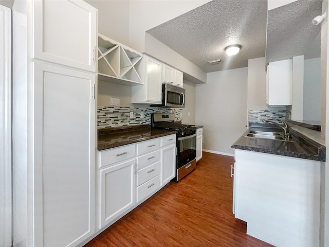 kitchen with stainless steel appliances, wood-type flooring, backsplash, sink, and white cabinets