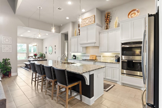 kitchen with white cabinets, appliances with stainless steel finishes, a kitchen island with sink, and pendant lighting