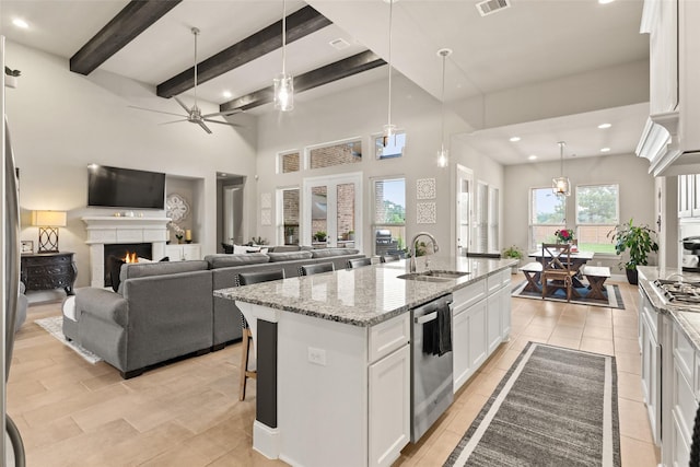 kitchen with light stone countertops, sink, white cabinetry, and an island with sink