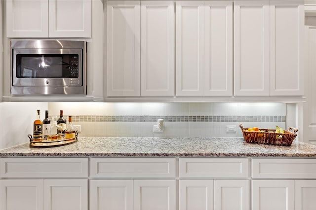 kitchen featuring light stone countertops, stainless steel microwave, and white cabinetry