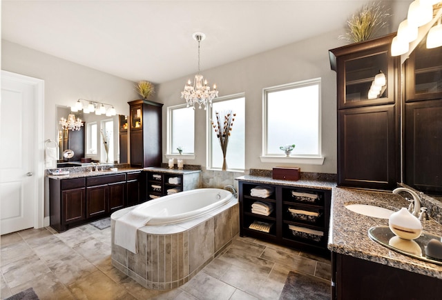 bathroom with vanity, a relaxing tiled tub, and an inviting chandelier