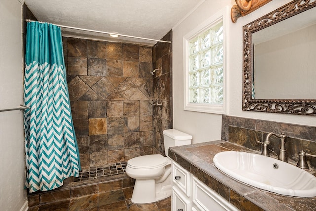 full bath featuring stone finish floor, a textured ceiling, vanity, toilet, and tiled shower