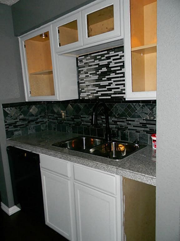 kitchen with sink, black dishwasher, backsplash, and white cabinetry