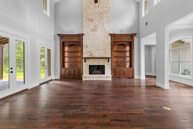 unfurnished living room featuring a high ceiling, a fireplace, built in shelves, and dark hardwood / wood-style flooring