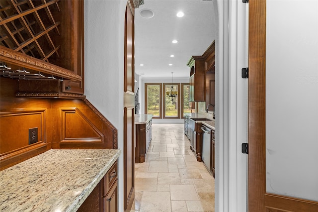 kitchen with light stone countertops, stainless steel dishwasher, light tile floors, and pendant lighting