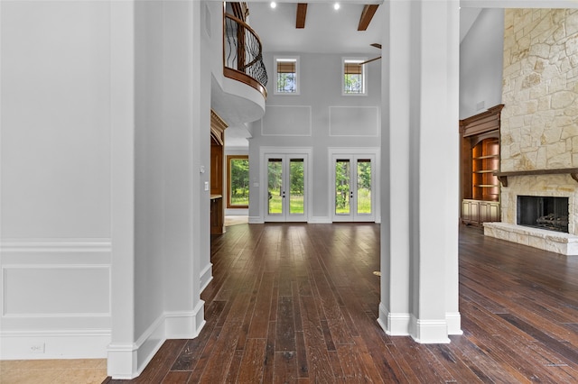 entrance foyer featuring beamed ceiling, dark hardwood / wood-style floors, a stone fireplace, a towering ceiling, and plenty of natural light