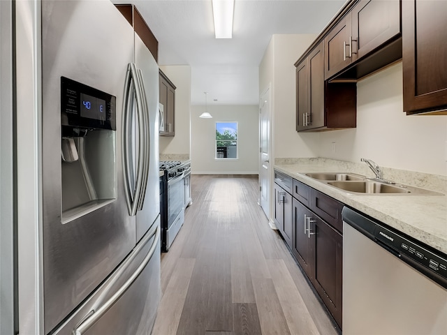 kitchen with light hardwood / wood-style floors, stainless steel appliances, dark brown cabinetry, hanging light fixtures, and sink