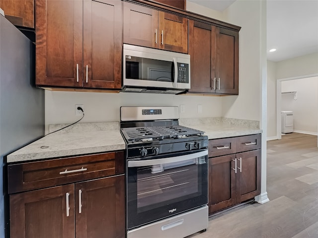 kitchen with appliances with stainless steel finishes, light hardwood / wood-style floors, dark brown cabinetry, and washer / clothes dryer