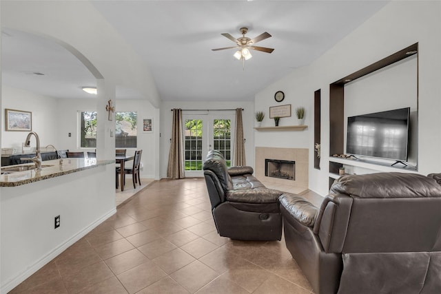 living room featuring sink, vaulted ceiling, light tile patterned floors, a tile fireplace, and ceiling fan