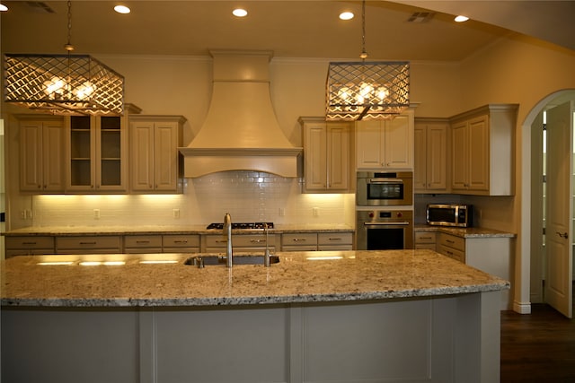 kitchen with custom range hood, a center island with sink, pendant lighting, and appliances with stainless steel finishes