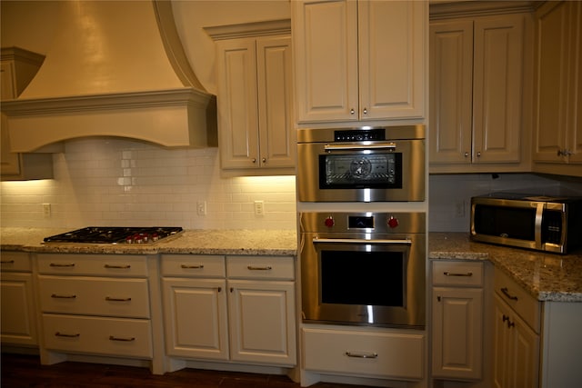 kitchen with dark hardwood / wood-style flooring, appliances with stainless steel finishes, premium range hood, light stone counters, and tasteful backsplash