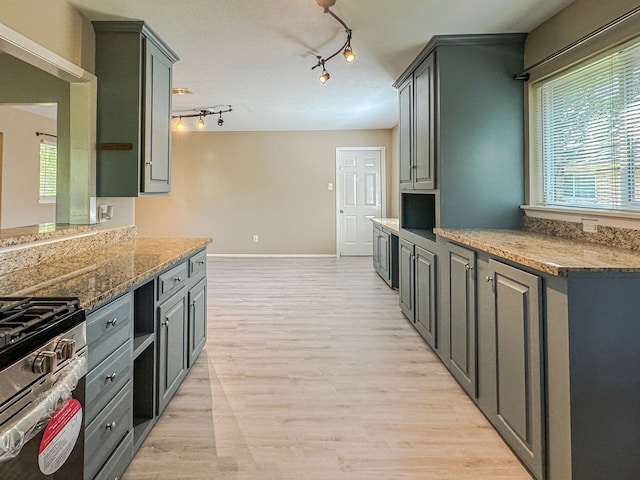 kitchen featuring stainless steel gas range oven, light stone counters, track lighting, and light wood-type flooring