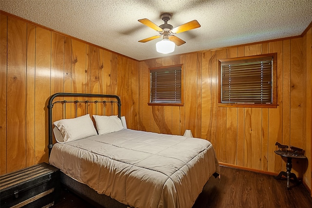 bedroom featuring a textured ceiling, ceiling fan, wood walls, and dark hardwood / wood-style flooring