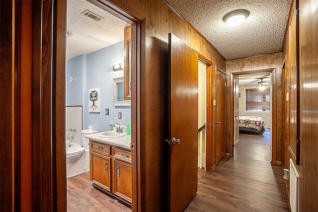 corridor featuring wooden walls, sink, a textured ceiling, and wood-type flooring