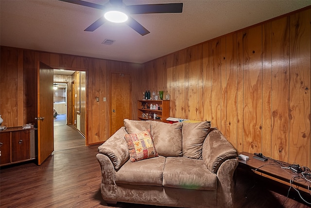 living room featuring dark wood-type flooring, wooden walls, ceiling fan, and a textured ceiling