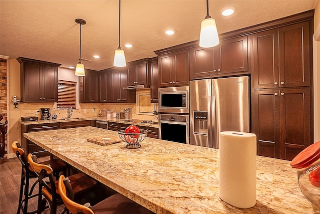 kitchen featuring light stone countertops, appliances with stainless steel finishes, dark hardwood / wood-style floors, decorative light fixtures, and tasteful backsplash