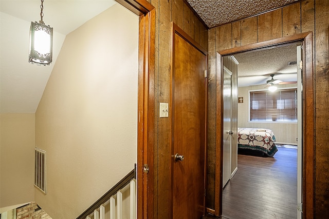 corridor featuring a textured ceiling, wooden walls, vaulted ceiling, and dark hardwood / wood-style flooring