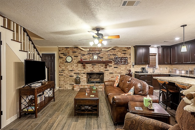 living room with brick wall, a brick fireplace, dark hardwood / wood-style floors, sink, and a textured ceiling