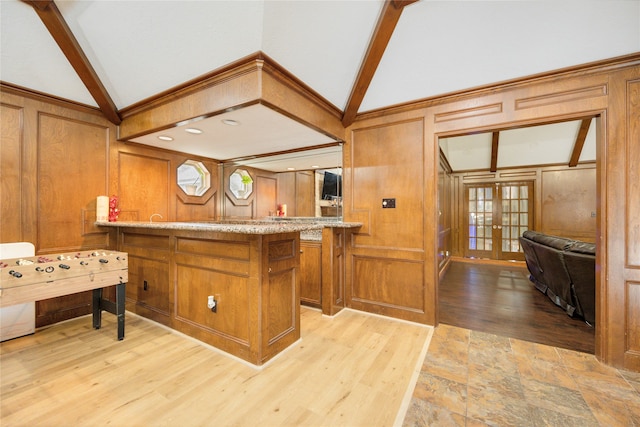 kitchen with french doors, vaulted ceiling with beams, light hardwood / wood-style flooring, wooden walls, and light stone counters