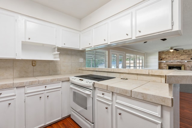 kitchen with ceiling fan, white electric range oven, dark hardwood / wood-style floors, a brick fireplace, and kitchen peninsula