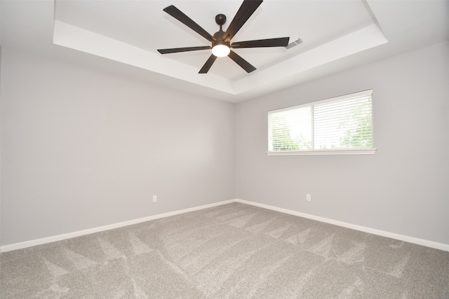 carpeted spare room with ceiling fan and a tray ceiling