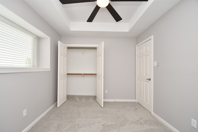 unfurnished bedroom with light carpet, a closet, ceiling fan, and a tray ceiling